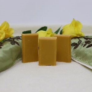 Photo shows three gold coloured By the Sea Soap Shoppe mini soap bars among green flowered towels and yellow roses. This soap contains clove, cinnamon, orange and patchouli essential oils, giving it an appealing, spicy scent. Vegan, natural ingredients, handmade in Prince Edward Island. $3.00 each