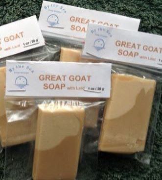 Picture of By the Sea Soap Shoppe Great Goat Soap Mini Soaps standing between green flowered towels with yellow roses in the background. Soap ingredients include goat milk and a "Honey, Milk and Oatmeal" fragrance. $3.00 each, 5 for $10.00